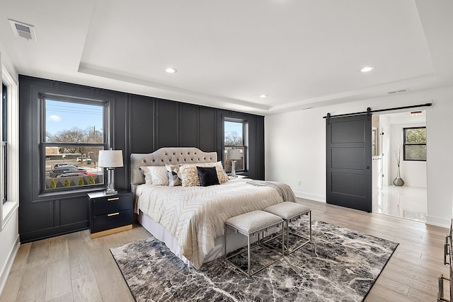 bedroom with a tray ceiling, a barn door, and light wood-type flooring