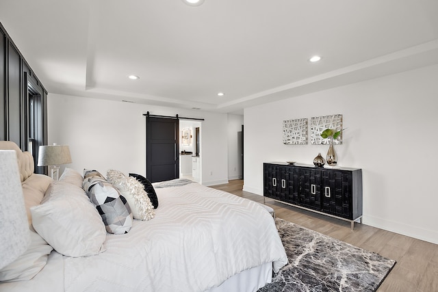 bedroom featuring a tray ceiling, wood-type flooring, and a barn door