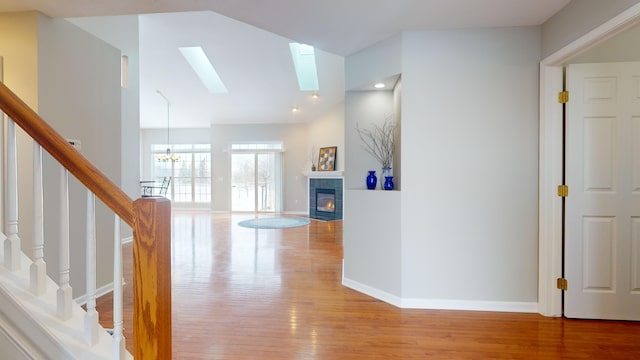 corridor with a skylight, a notable chandelier, high vaulted ceiling, and light hardwood / wood-style flooring