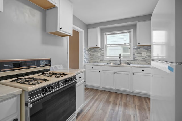 kitchen with sink, white appliances, white cabinets, and light wood-type flooring