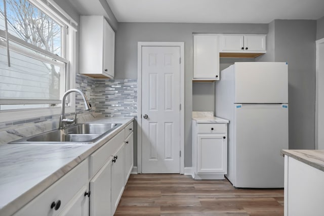 kitchen with sink, white refrigerator, white cabinets, and light wood-type flooring