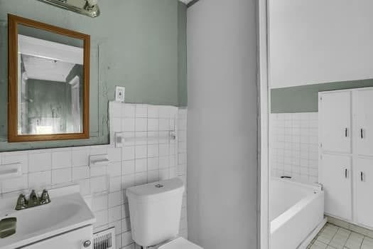 bathroom featuring tile walls, tile patterned flooring, vanity, a bath, and toilet