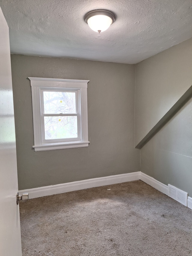 empty room featuring a textured ceiling, visible vents, baseboards, and carpet floors