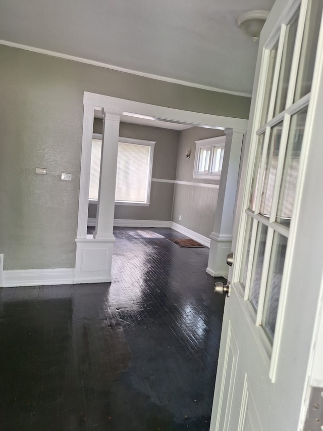empty room with baseboards, dark wood-style flooring, ornamental molding, and ornate columns