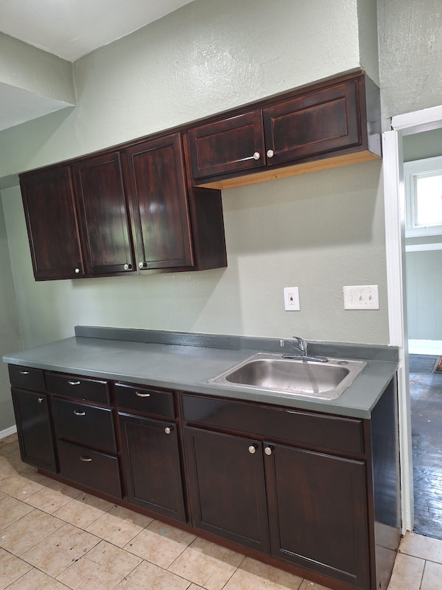 kitchen with a sink, dark brown cabinetry, light tile patterned flooring, and a textured wall