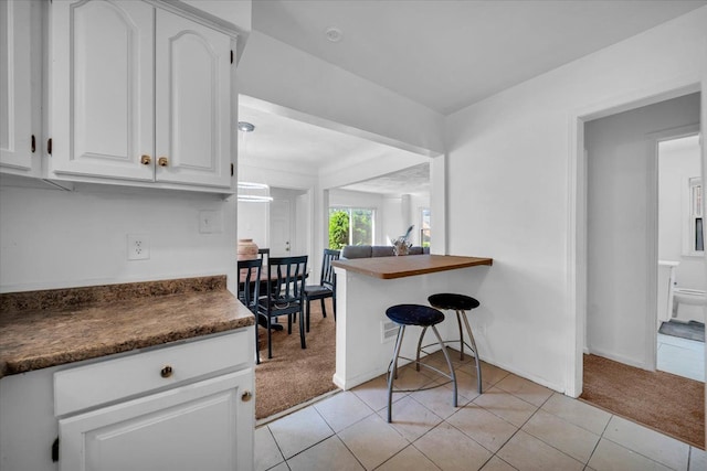 kitchen with light carpet, dark countertops, light tile patterned floors, and white cabinets