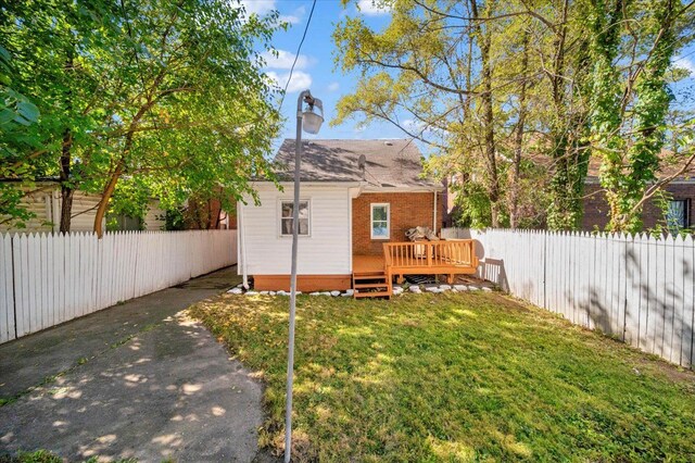 rear view of property featuring a deck, a yard, brick siding, and a fenced backyard