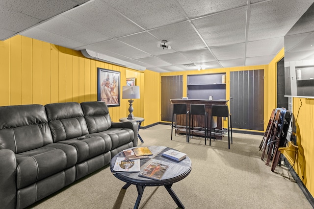 living room with carpet floors, a drop ceiling, bar area, and wooden walls