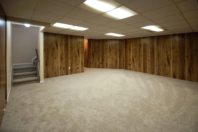 basement with wooden walls, a paneled ceiling, and carpet