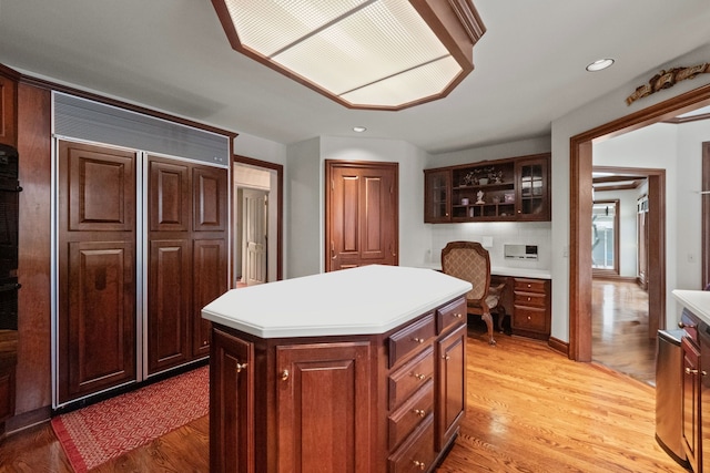 kitchen featuring a kitchen island, light wood-style floors, light countertops, built in desk, and glass insert cabinets