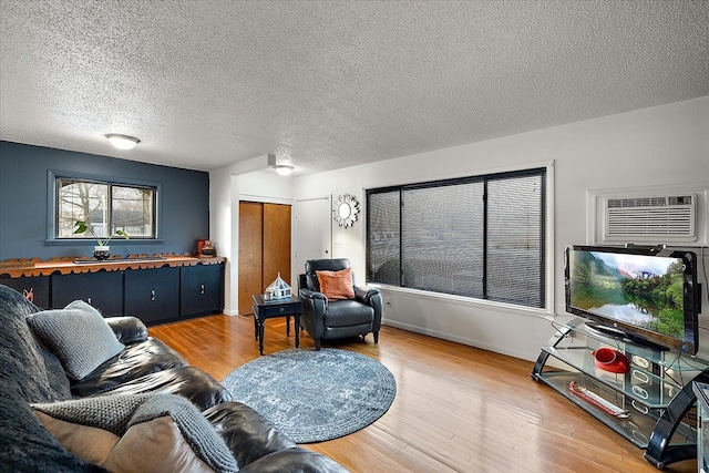 living room with hardwood / wood-style floors, a wall mounted AC, and a textured ceiling