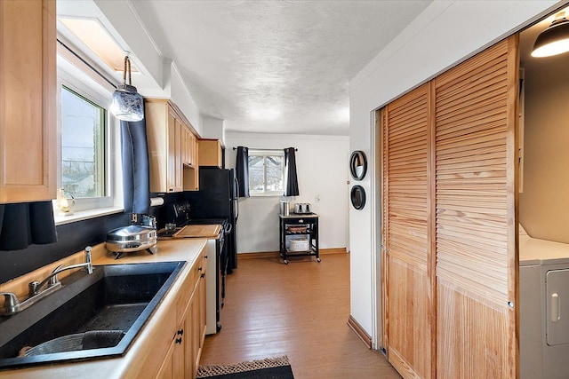 kitchen with electric stove, light brown cabinetry, sink, and hanging light fixtures