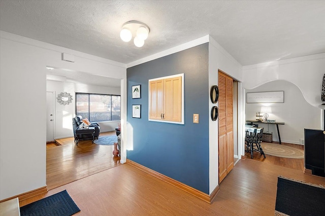 hallway featuring ornamental molding, a textured ceiling, and light wood-type flooring