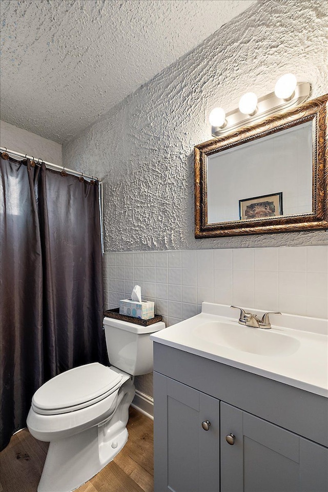 bathroom with hardwood / wood-style floors, tile walls, vanity, toilet, and a textured ceiling