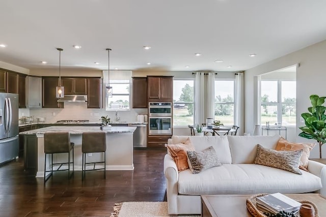 kitchen with hanging light fixtures, stainless steel appliances, dark hardwood / wood-style floors, a center island, and light stone countertops