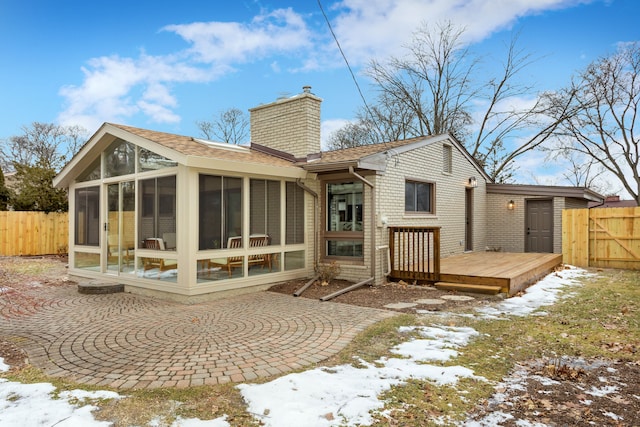 snow covered rear of property with a wooden deck and a sunroom