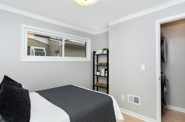 bedroom featuring ornamental molding, stacked washer and clothes dryer, and light hardwood / wood-style floors