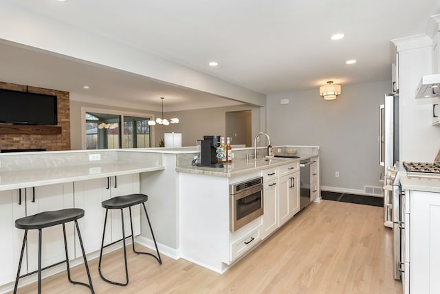 kitchen featuring sink, light hardwood / wood-style flooring, appliances with stainless steel finishes, white cabinetry, and a kitchen bar