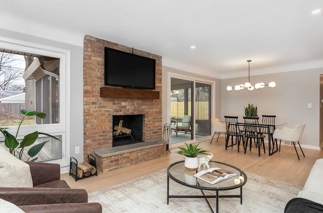 living room featuring a healthy amount of sunlight, an inviting chandelier, a fireplace, and light hardwood / wood-style flooring