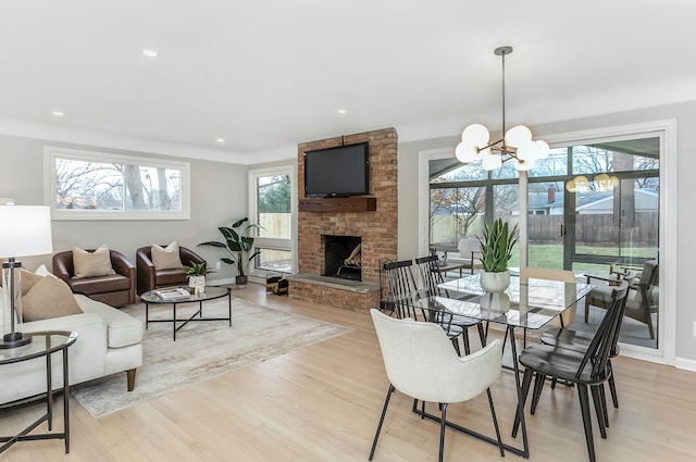 dining area featuring light hardwood / wood-style floors, a brick fireplace, and a notable chandelier