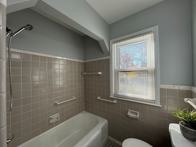 bathroom with tiled shower / bath, tile walls, and toilet