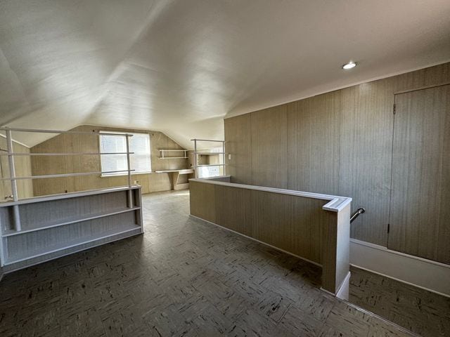 additional living space featuring vaulted ceiling and wooden walls