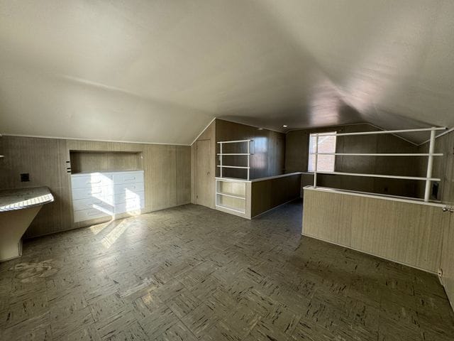 bonus room with lofted ceiling, wooden walls, and built in features