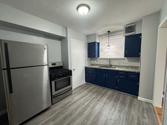 kitchen with wood-type flooring, appliances with stainless steel finishes, sink, and blue cabinetry