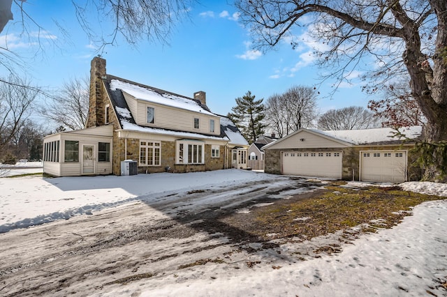 snow covered rear of property featuring a garage, a sunroom, and central air condition unit