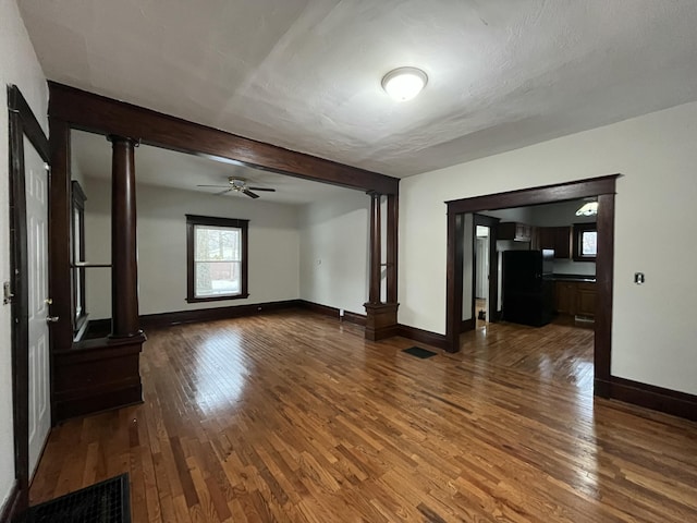 unfurnished living room with decorative columns, hardwood / wood-style floors, ceiling fan, and beamed ceiling