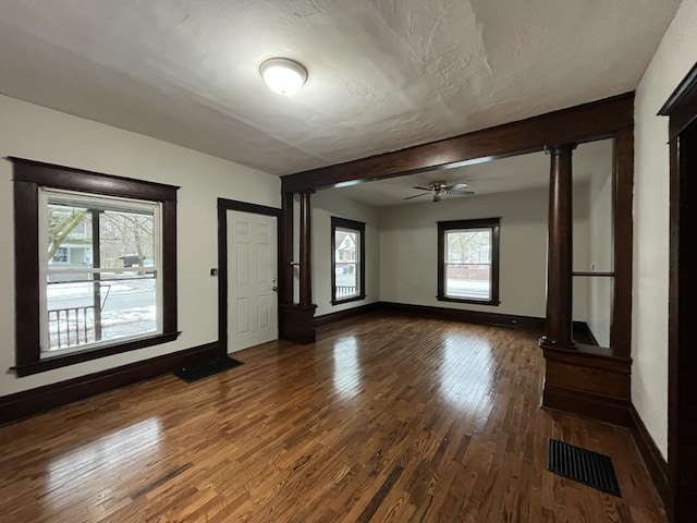 unfurnished living room with ornate columns, hardwood / wood-style floors, beamed ceiling, ceiling fan, and a textured ceiling