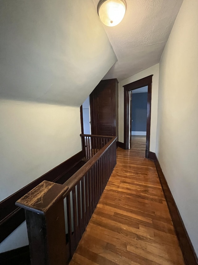 corridor featuring vaulted ceiling, a textured ceiling, and dark hardwood / wood-style flooring