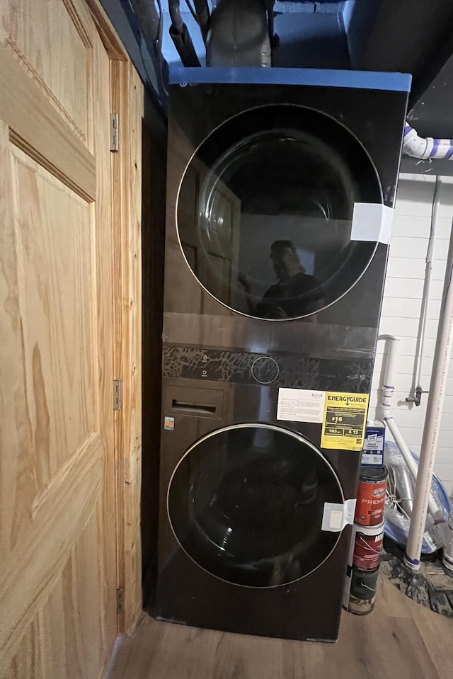 laundry room with hardwood / wood-style flooring and stacked washer and clothes dryer