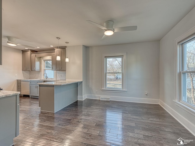 kitchen featuring dark wood-type flooring, light stone counters, tasteful backsplash, kitchen peninsula, and pendant lighting