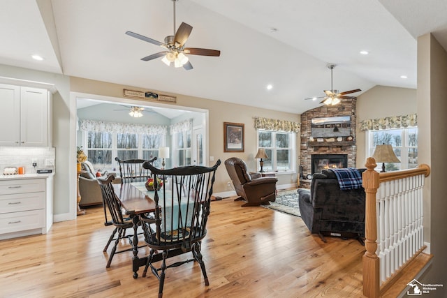 dining room featuring ceiling fan, lofted ceiling, a stone fireplace, and light wood-type flooring