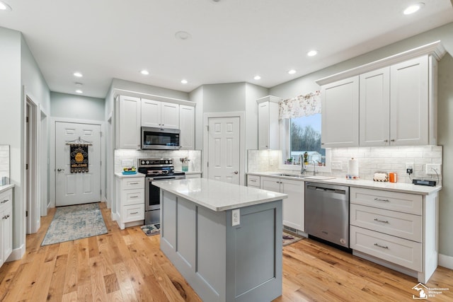 kitchen featuring a kitchen island, sink, white cabinets, stainless steel appliances, and light hardwood / wood-style flooring