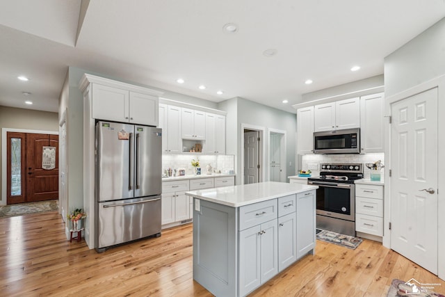 kitchen with backsplash, stainless steel appliances, light hardwood / wood-style floors, white cabinets, and a kitchen island