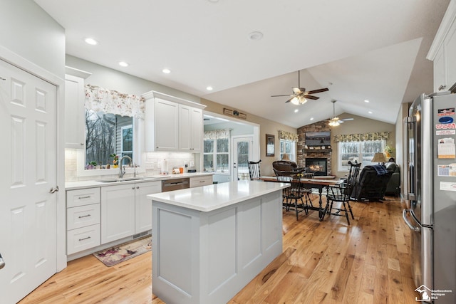 kitchen featuring lofted ceiling, sink, appliances with stainless steel finishes, white cabinetry, and a stone fireplace