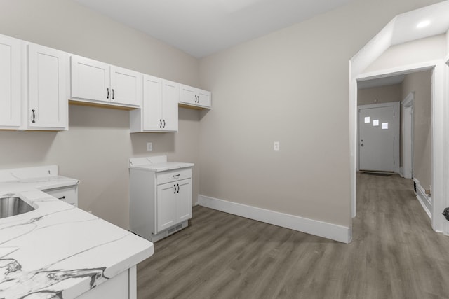 kitchen with white cabinetry, light stone counters, and light wood-type flooring