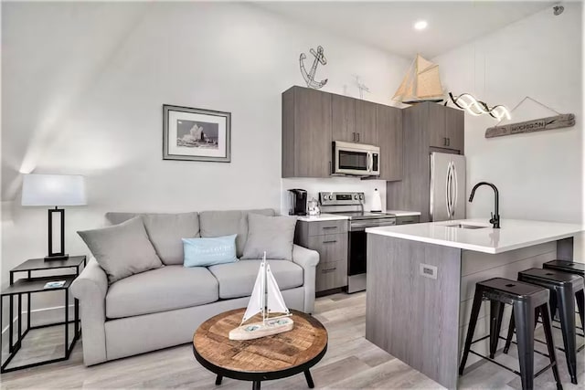 kitchen with sink, a breakfast bar area, dark brown cabinetry, stainless steel appliances, and light wood-type flooring