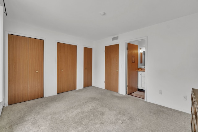 unfurnished bedroom with light carpet, two closets, and ensuite bath