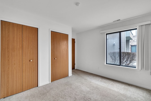 unfurnished bedroom with light colored carpet and two closets