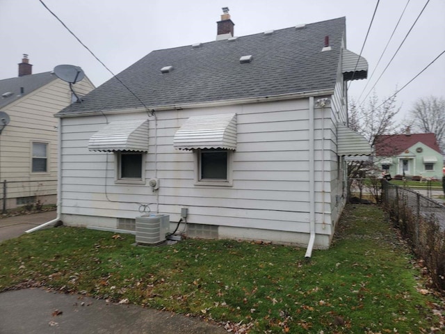 rear view of house featuring central AC unit and a lawn