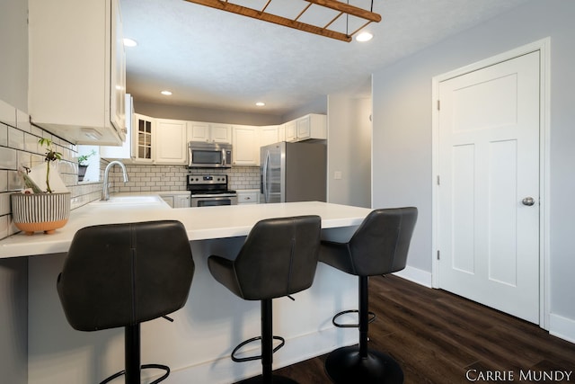 kitchen with a kitchen breakfast bar, kitchen peninsula, white cabinets, and appliances with stainless steel finishes