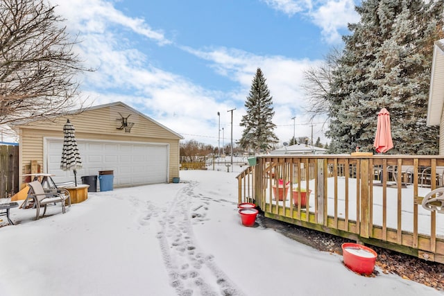 snowy yard with a wooden deck, a garage, and an outdoor structure