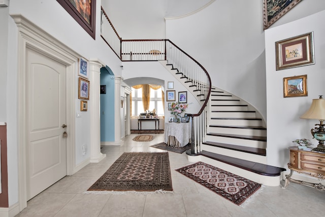 foyer entrance featuring light tile patterned flooring, a towering ceiling, and ornate columns