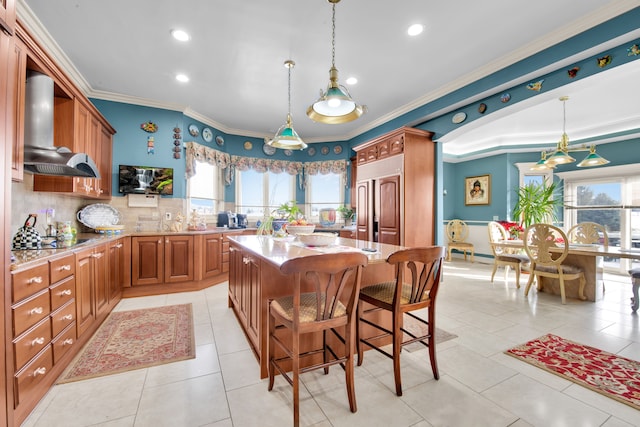 kitchen featuring a breakfast bar area, a center island, wall chimney range hood, and decorative light fixtures