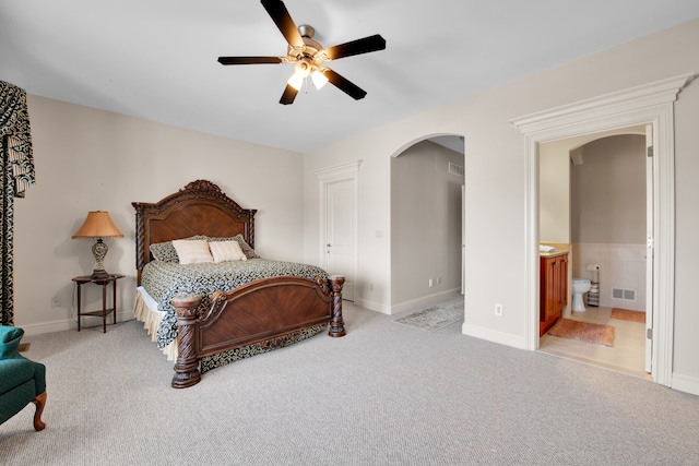 bedroom with light carpet, ensuite bath, and ceiling fan