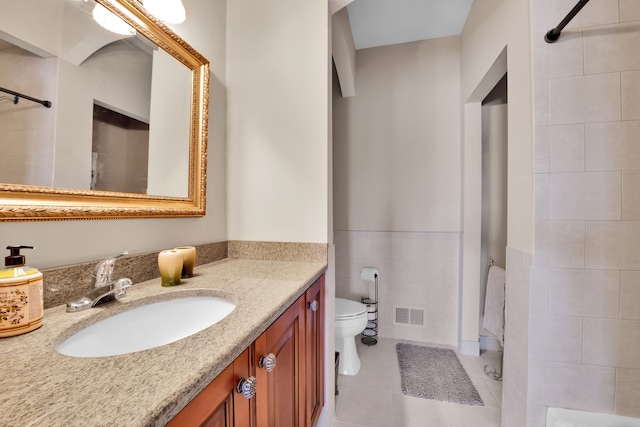 bathroom featuring tile walls, vanity, a tile shower, tile patterned floors, and toilet