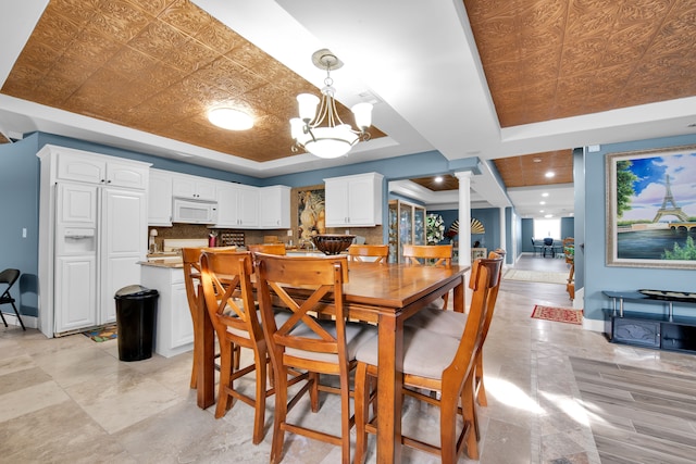 dining space featuring decorative columns, an inviting chandelier, and a tray ceiling